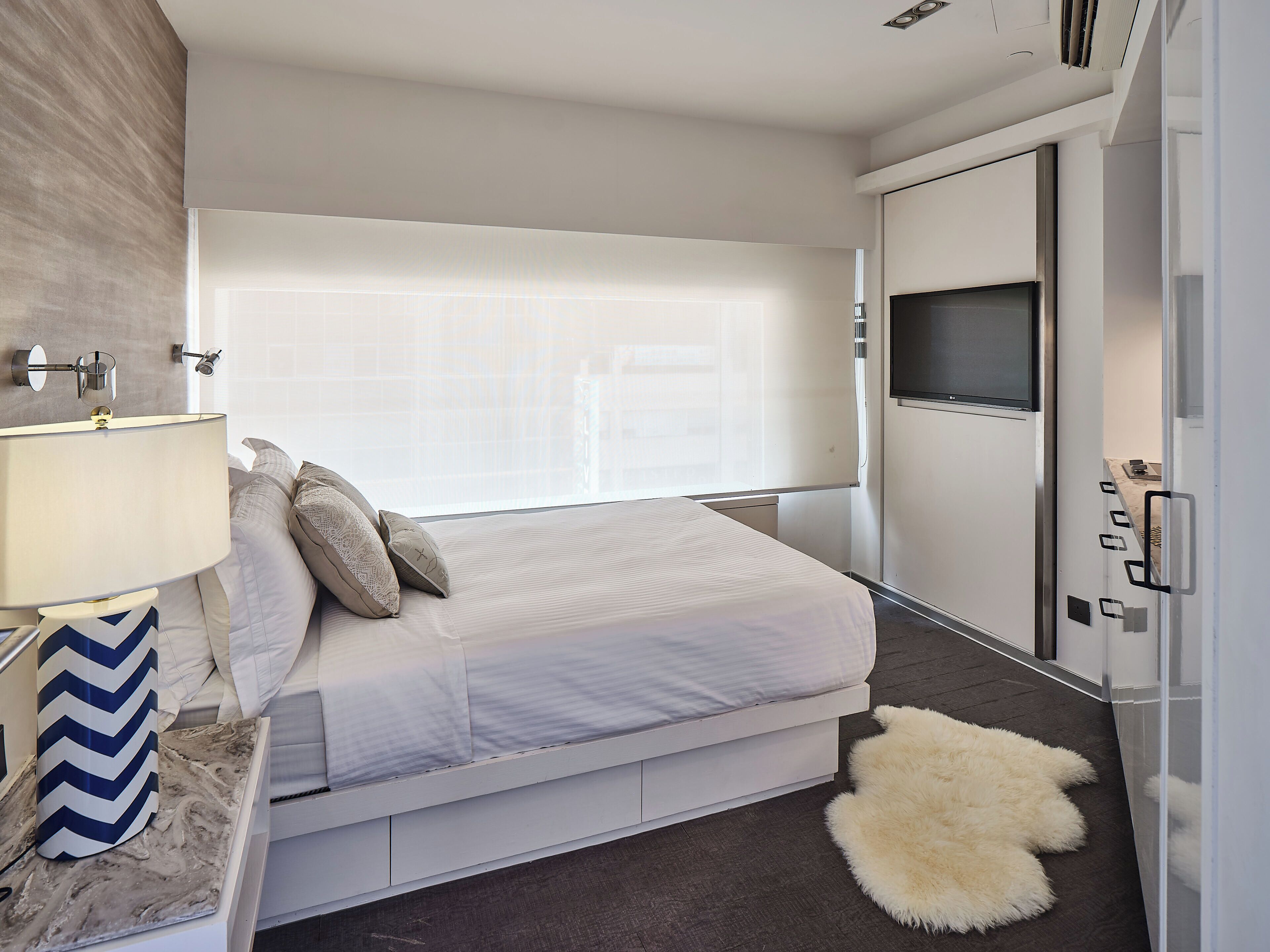 A modern bedroom with a bed, a TV, and a large window.
