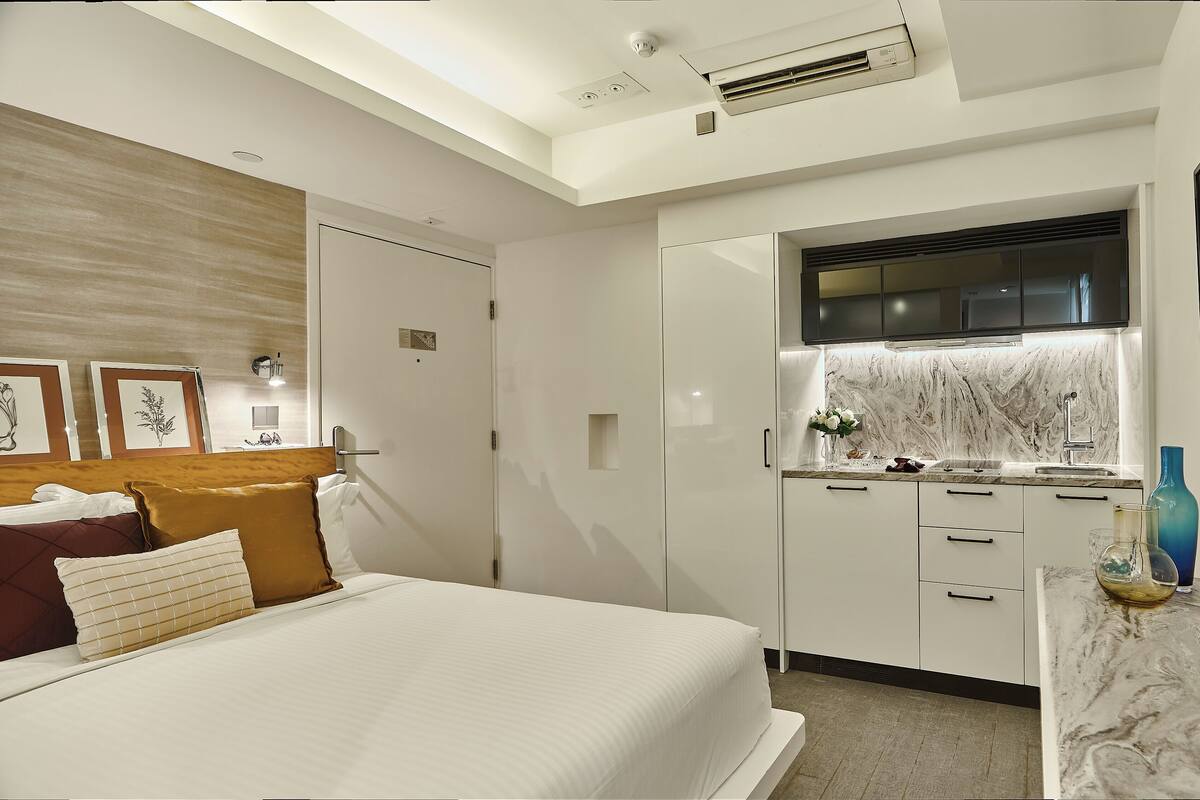 A modern bedroom with a large bed, a built-in wardrobe, and a small kitchenette.
