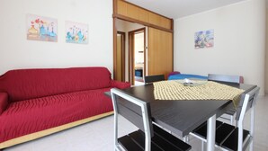 A compact living space with a red sofa, a small dining table with chairs, and a kitchenette visible through an open door. - 1 bedroom beautiful apartment in Parco dei Tigli (Parco dei Tigli)