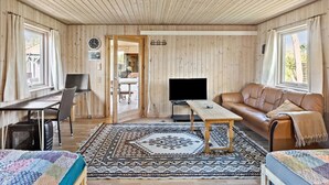 A cozy room with wooden walls and ceiling, a leather sofa, a wooden table, a TV, and a patterned rug. - Nice home in Gedser with kitchen (Gedser)