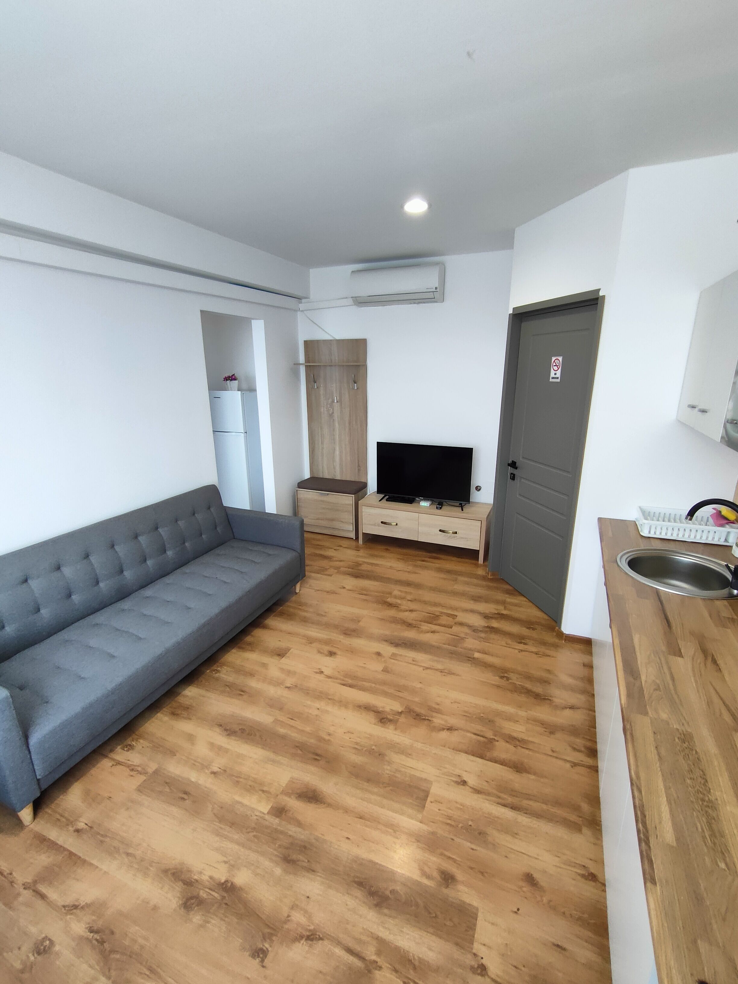 Un espacio habitable compacto con sofá, televisor, mueble de madera y una zona de cocina con lavabo.