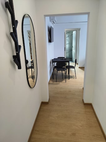 A hallway with a dining area featuring a table and chairs, a large mirror, and a television mounted on the wall.