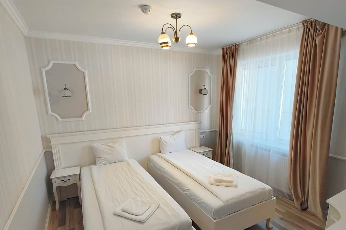 A hotel room with two beds, a ceiling light fixture, and a large window with curtains.
