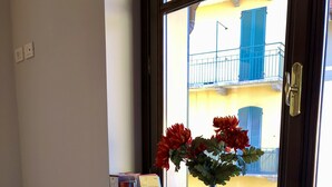 A room with a white sofa, a window with a view of a balcony, and a vase with flowers on the windowsill.