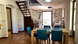 A dining area with a wooden table and blue chairs, a staircase, and a view of a dog through a glass door.