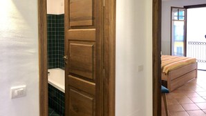 A hallway with a wooden door leading to a bathroom with green tiles and a white bathtub.