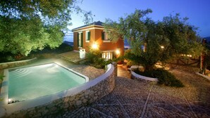 Una villa con piscina, sendero de piedra y abundante vegetación.