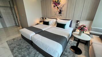 Een moderne hotelkamer met een groot bed, twee nachtkastjes, een klein rond tafeltje met een bloevas en een decoratief wandobject.