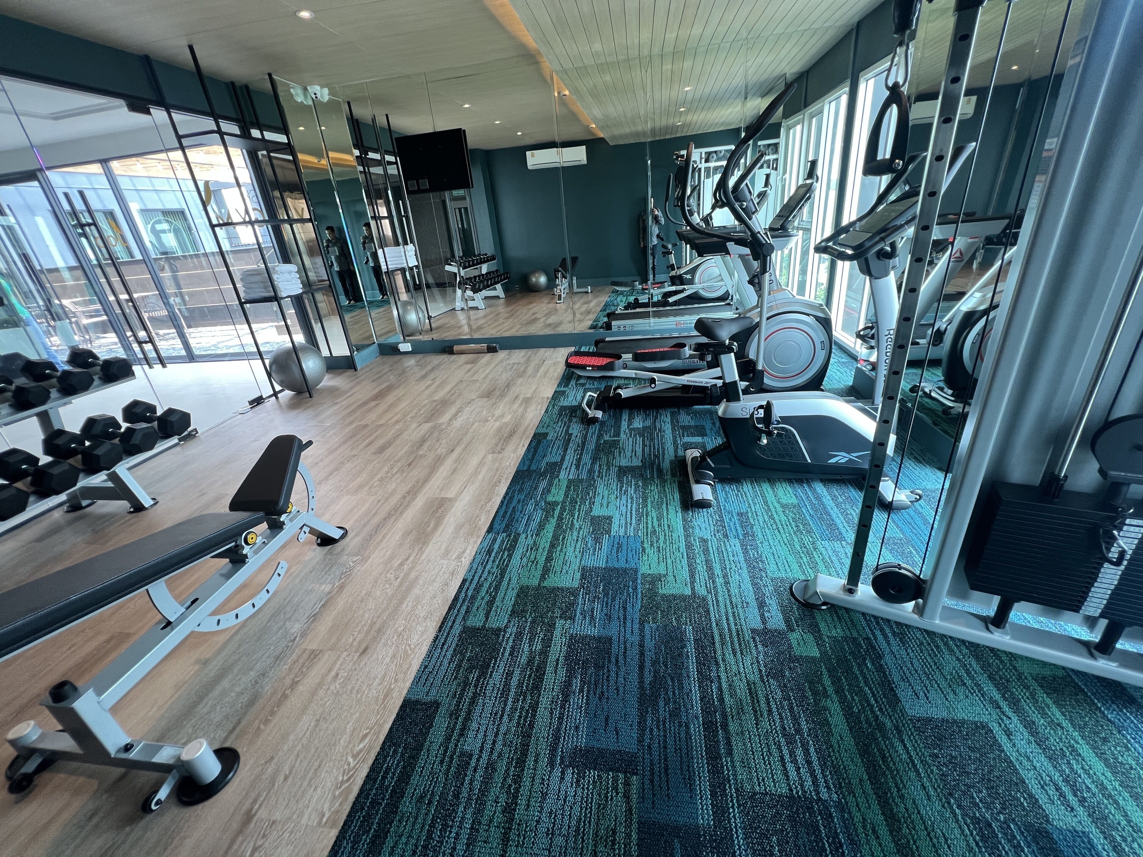 A gym with exercise equipment, a wooden floor, and large windows.