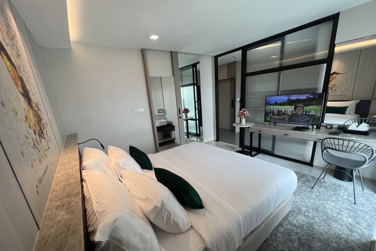 A modern hotel room with a large bed, a desk, a chair, a TV, and a large window.