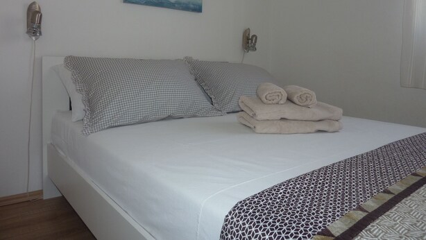 A neatly made bed with a checkered pillow, a rolled towel, and a patterned throw.