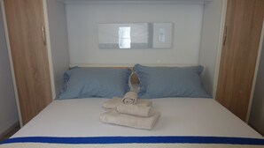 A neatly made bed with blue pillows, a blue and white striped bedspread, and a folded towel on the bed.