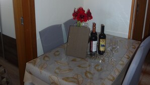 A dining table with a leaf-patterned tablecloth, two wine bottles, and a vase with red flowers.