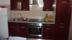 A compact kitchen with dark red cabinets, stainless steel appliances, and a fruit bowl on the counter.