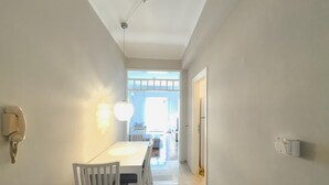 A hallway with a dining area featuring a white table and chairs, a chandelier, and a wall-mounted telephone. - Dionysos - Acropolis Residence Apartment (Athens)
