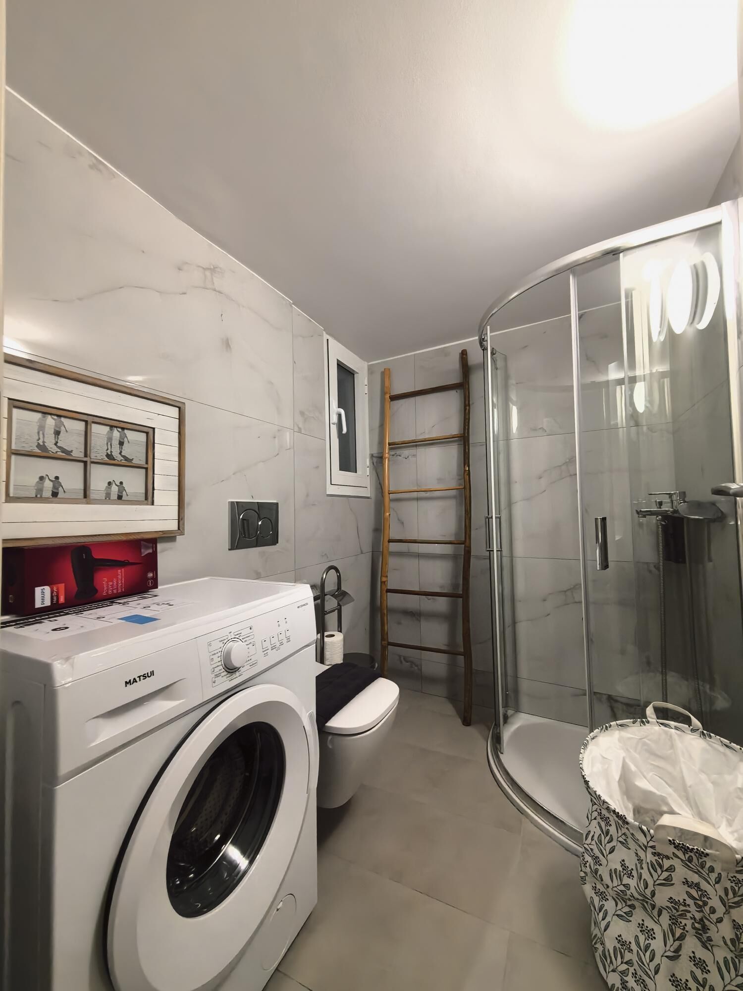 A compact bathroom with a washing machine, toilet, and glass shower enclosure.