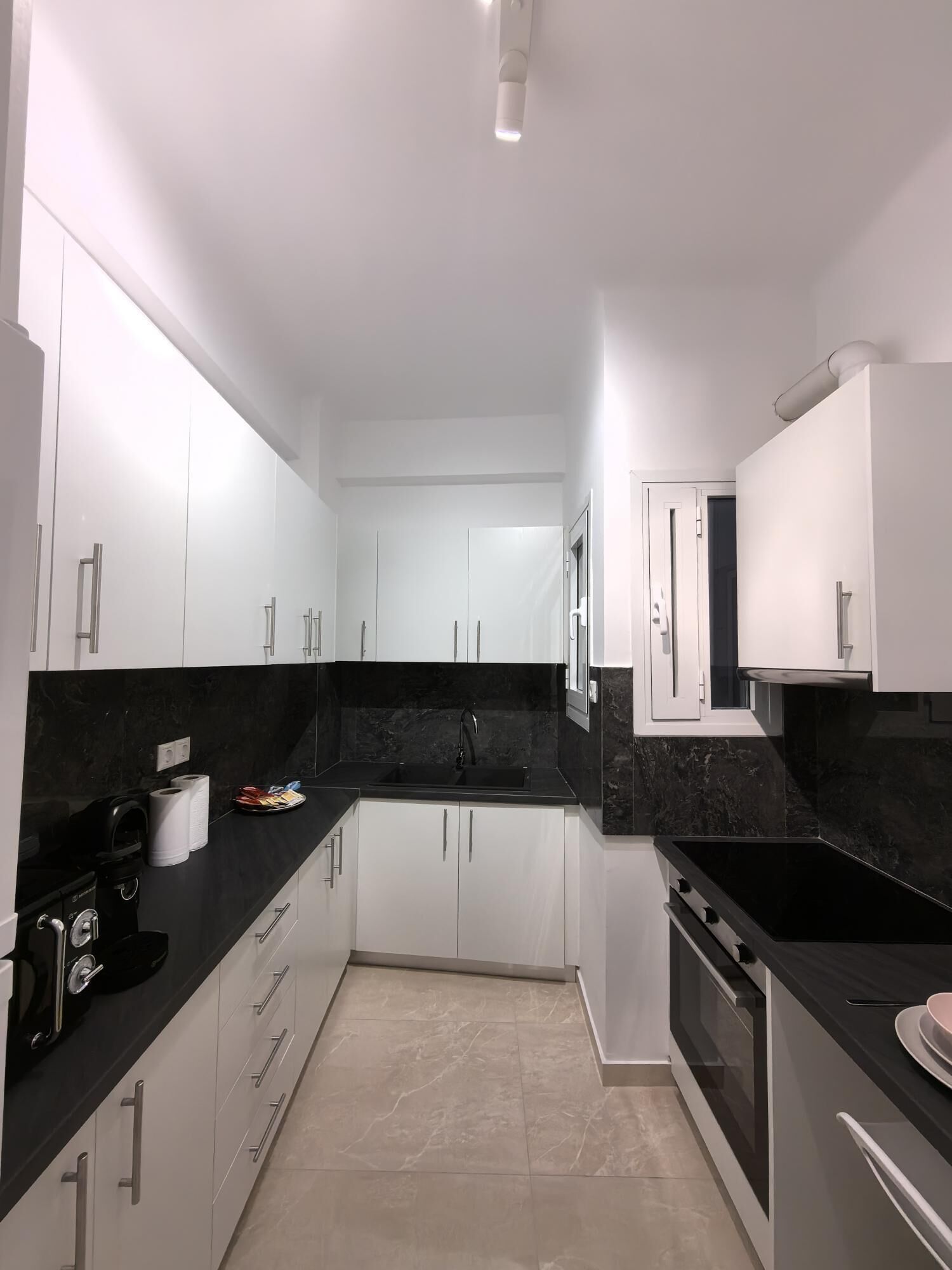A modern kitchen with white cabinets, black countertops, a black stove, and a sink.