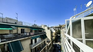 Un immeuble à plusieurs étages doté de balcons, une rue étroite en contrebas et un ciel bleu dégagé.
