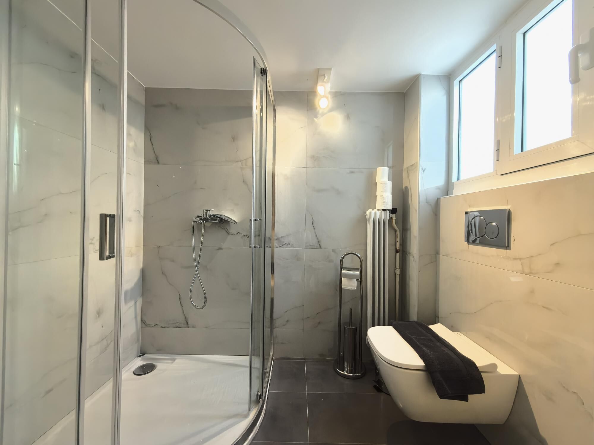 Un baño moderno con ducha acristalada, inodoro y toalla, además de un radiador.