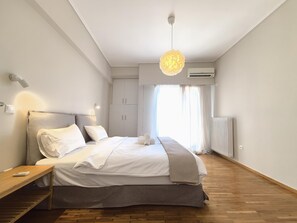 A modern bedroom with a large bed, bedside tables, a hanging light fixture, and an air conditioning unit. - Apollon - Acropolis Residence Apartment (Athens)