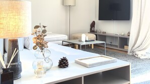 Un salon moderne avec un téléviseur à écran plat, un canapé blanc, une table basse et une lampe.