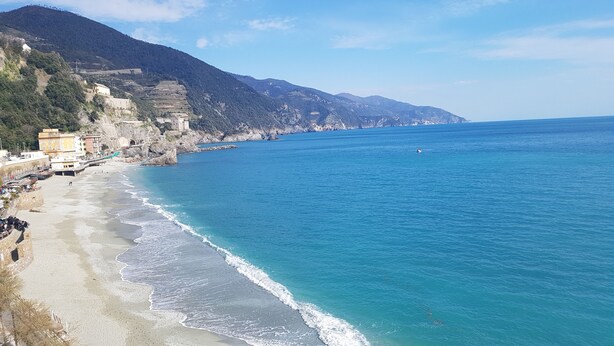 Une plage côtière avec un rivage rocheux, des bâtiments le long de la côte et une chaîne de montagnes en arrière-plan.
