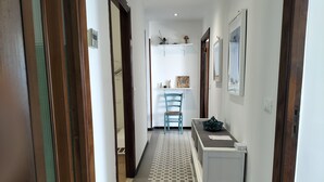 Un couloir avec un sol à carreaux, une chaise, une petite table et un meuble.