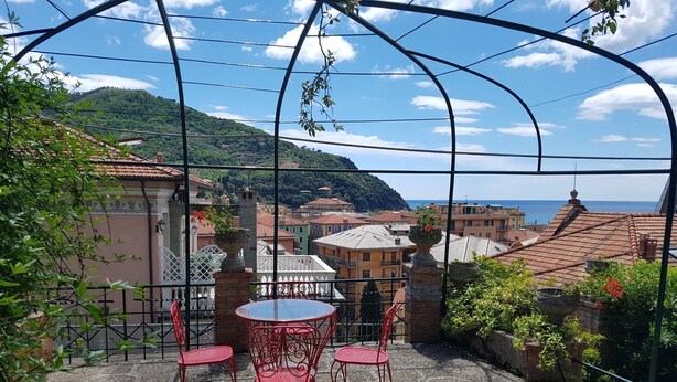 A terrace with a table and chairs, overlooking a coastal town with buildings and a hill in the background. - Benedetta Beautiful House - By the Sea with A/C (Levanto)
