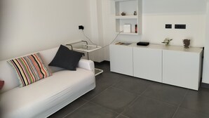 A modern living space with a white sofa, a glass coffee table, a white cabinet, and a black shelf.