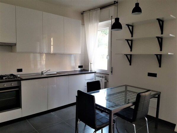 Une cuisine moderne avec des meubles blancs, une cuisinière à gaz, un évier et une table à manger en verre, accompagnée de chaises.