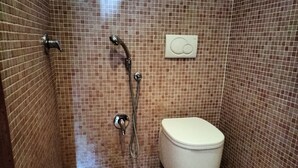 Ett badrum med en kaklad dusch, en toalett och en väggmonterad kontrollpanel.