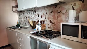 Ett kök med vita skåp, en gasspis, en mikrovågsugn och ett kaklat stänkskydd.