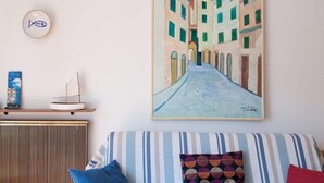 A room with a striped sofa, a framed painting of a street, a small ship model, and a wall clock.