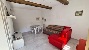 A compact living space with a red sofa, a small dining table with chairs, and a white cabinet.