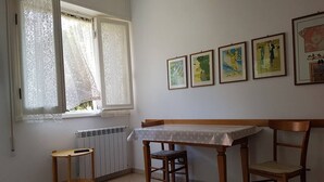 A room with a dining table, two chairs, a small side table, and a radiator. There are four framed pictures on the wall. - Giuliana Cosy Apt central & near the best beaches (Monterosso al Mare)