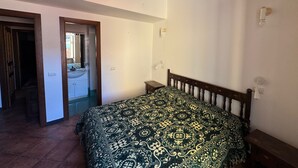 Une chambre à coucher avec un lit en bois, une table de chevet, un miroir et une porte donnant sur une salle de bain.