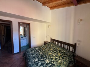 Une chambre à coucher avec un lit en bois, une table de chevet, un miroir et une porte donnant sur une salle de bain.