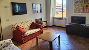 Un salon avec un canapé, une table en bois, un téléviseur et une fenêtre donnant sur des immeubles.