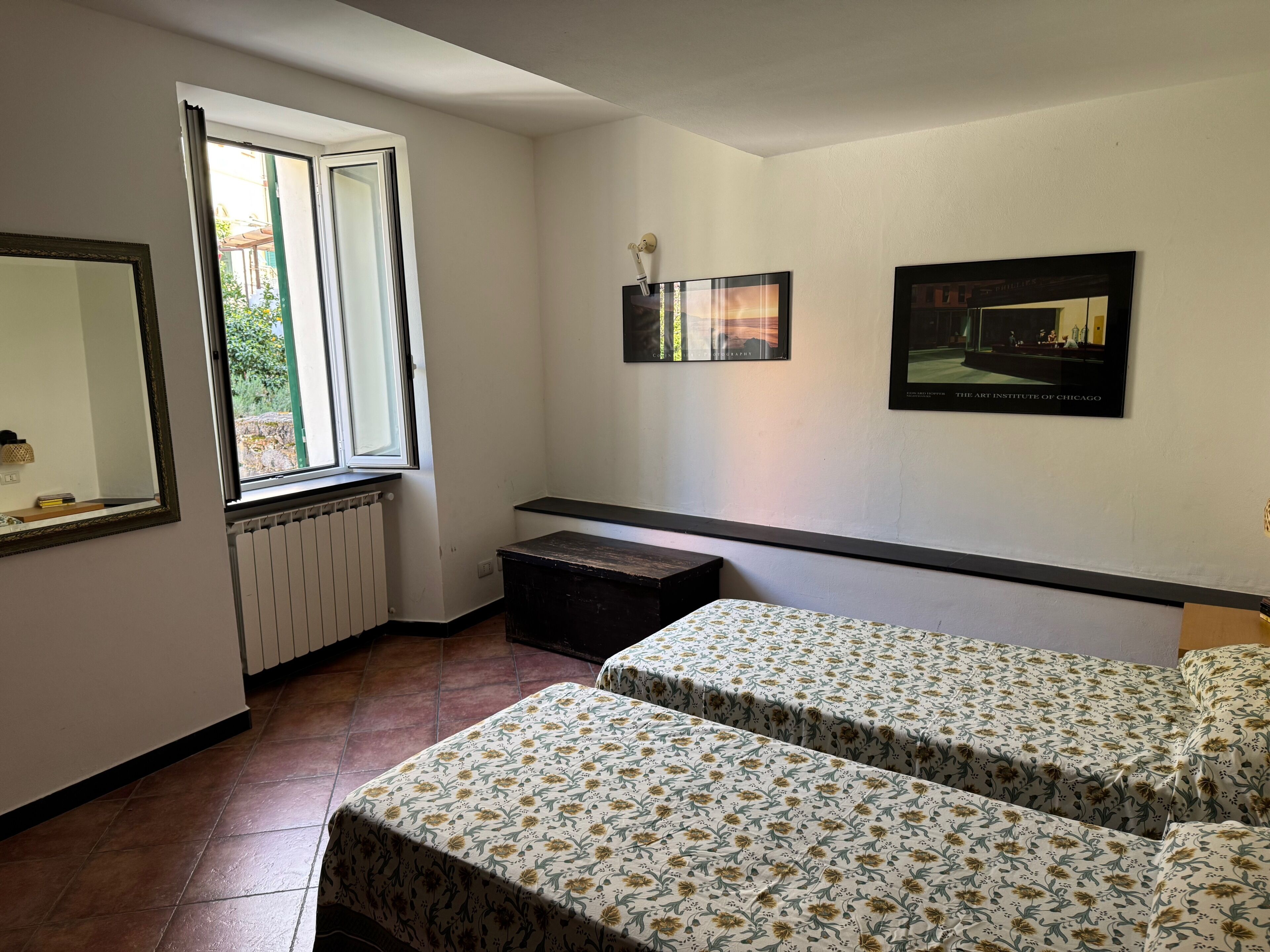 Une chambre avec deux lits, un radiateur, une fenêtre et deux tableaux encadrés accrochés au mur.