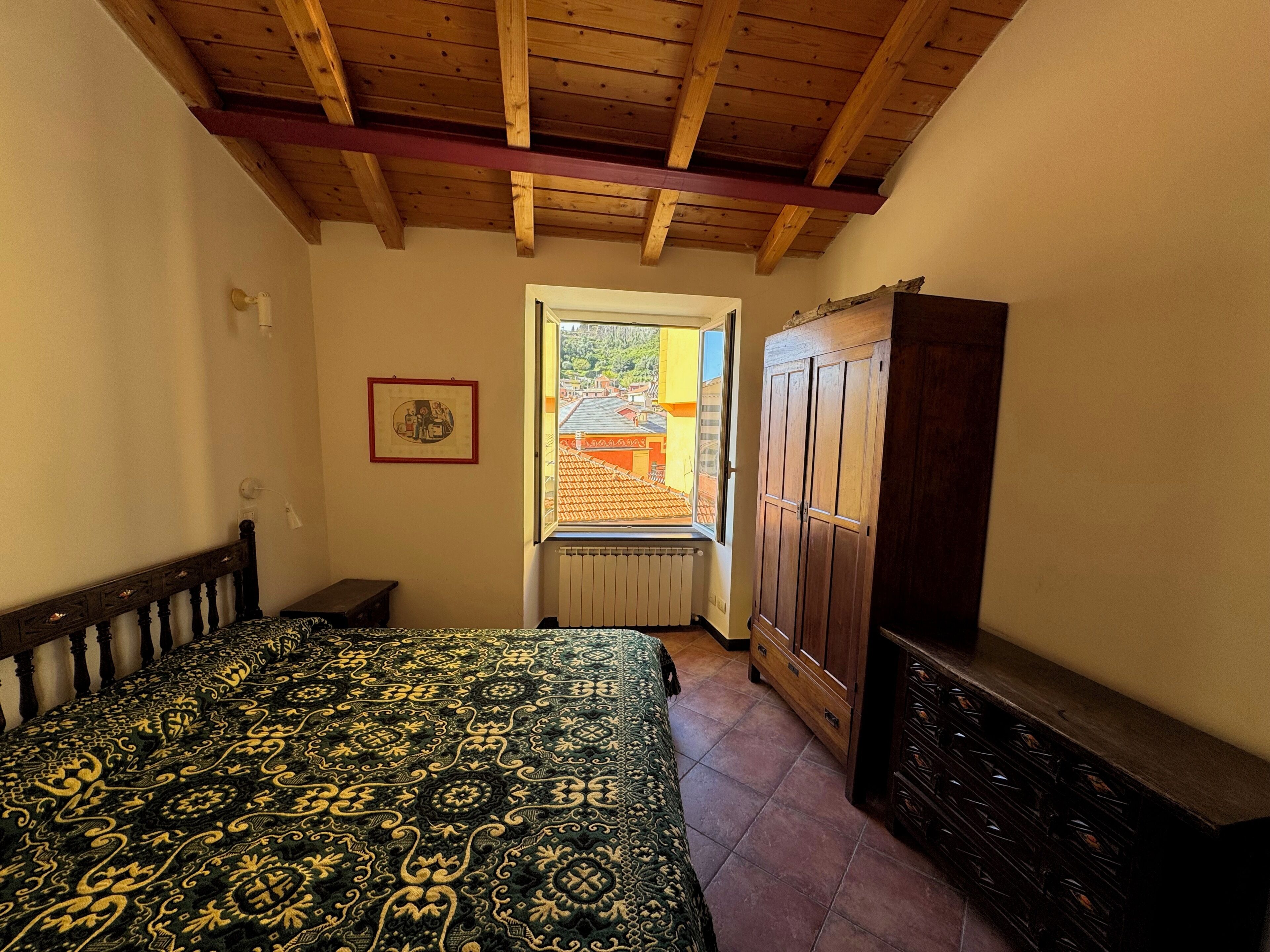 Ein Schlafzimmer mit einem Bett, einem Kleiderschrank, einem Heizkörper und einem Fenster mit Blick auf ein Gebäude.