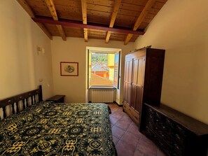 Een slaapkamer met een bed, een kledingkast, een radiator en een raam met uitzicht op een gebouw.