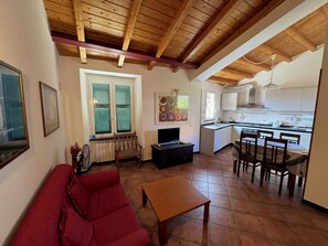 Un salon avec un canapé rouge, une table en bois et un téléviseur. Il y a également un coin cuisine avec des placards et une table à manger.