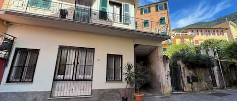 A two-story building with a balcony, a stone-paved courtyard, and a mountain in the background.