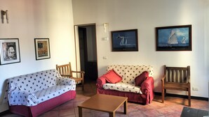 Un salon avec un canapé rouge, un canapé à motifs et une table en bois. On y trouve deux fauteuils, un téléviseur et des tableaux encadrés accrochés au mur.