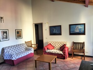 Un salon avec un canapé rouge, un canapé à motifs et une table en bois. On y trouve deux fauteuils, un téléviseur et des tableaux encadrés accrochés au mur.