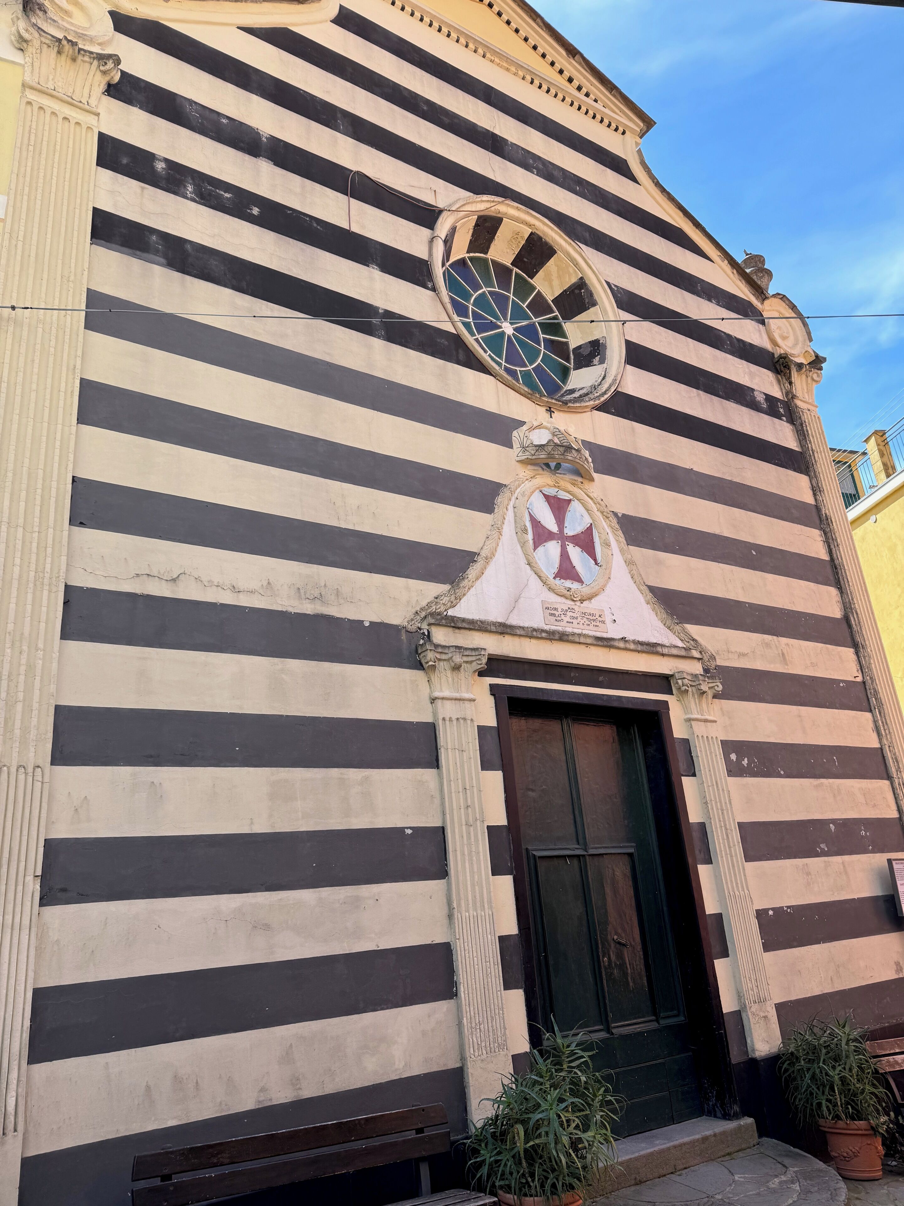 A building with a striped facade, a circular window, and a door with a cross symbol.