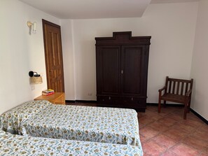 Une chambre avec deux lits, une armoire, un banc et une lampe fixée au mur.