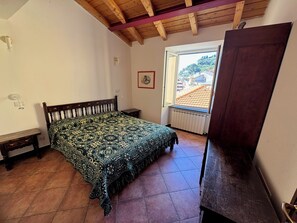 Une chambre à coucher avec un lit, une tête de lit en bois, une fenêtre donnant sur un paysage agréable, un radiateur et une armoire en bois.
