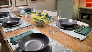 A dining table set with black plates, clear glasses, and a vase of yellow flowers.