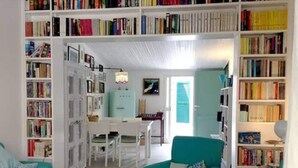 A cozy living room with teal armchairs, a dining table, and a bookshelf filled with books.